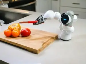 A humanoid robot uses modern technology to slice tomatoes on a wooden chopping board.